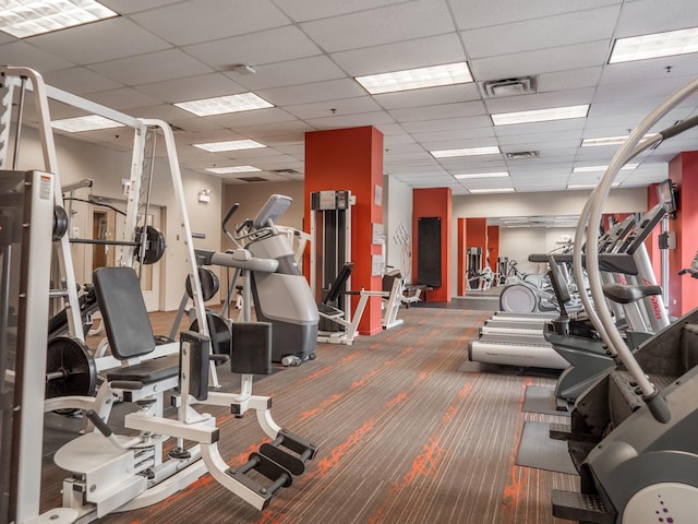 gym with a paneled ceiling and dark carpet