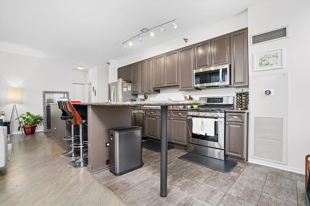 kitchen with a breakfast bar area, light wood-type flooring, appliances with stainless steel finishes, light stone countertops, and backsplash