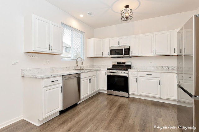 kitchen with sink, hanging light fixtures, light wood-type flooring, stainless steel appliances, and white cabinets