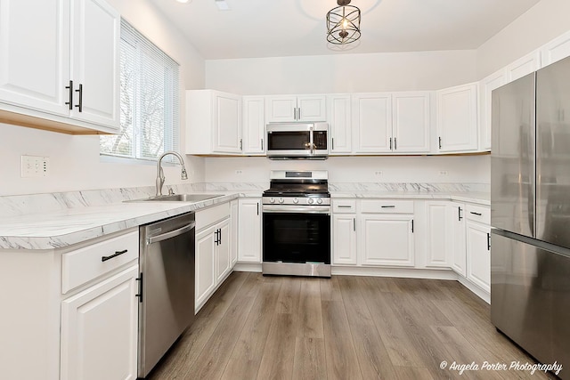 kitchen with light hardwood / wood-style floors, sink, appliances with stainless steel finishes, white cabinets, and a chandelier