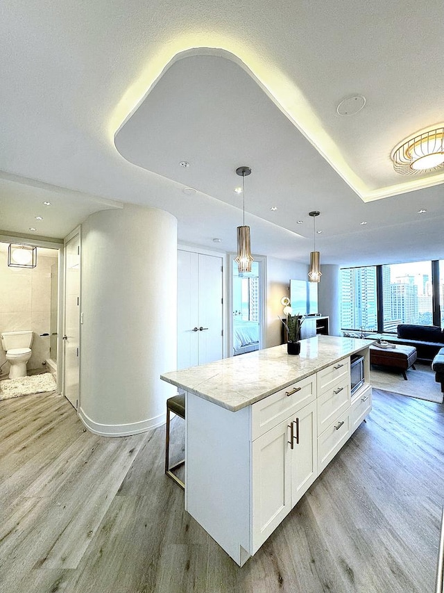 kitchen with light stone countertops, a kitchen island, white cabinetry, hanging light fixtures, and light wood-type flooring