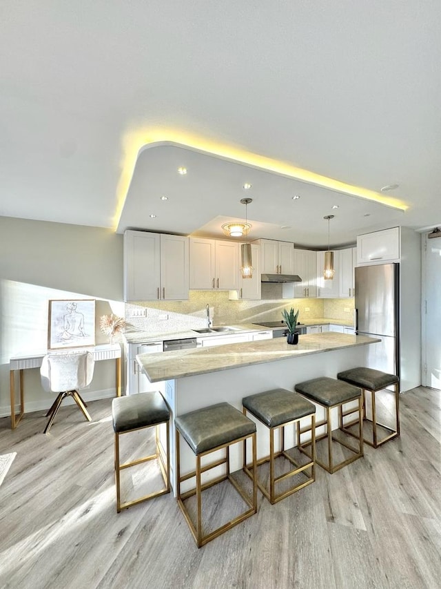 kitchen with white cabinets, stainless steel fridge, hanging light fixtures, and sink