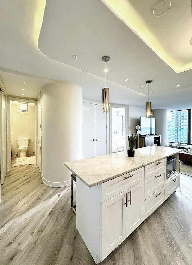 kitchen featuring light hardwood / wood-style floors, a kitchen island, white cabinetry, hanging light fixtures, and light stone countertops