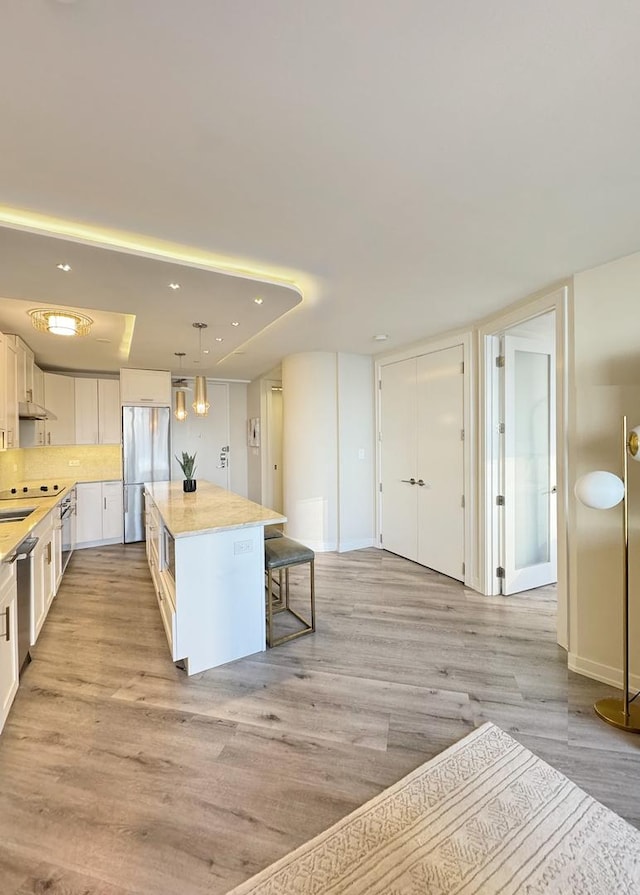 kitchen with decorative light fixtures, a kitchen island, white cabinetry, a kitchen breakfast bar, and stainless steel appliances