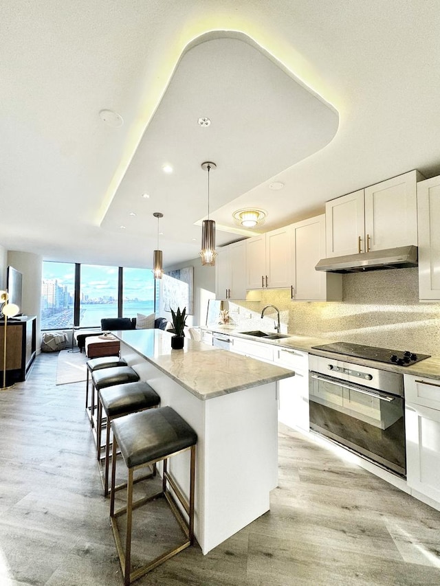 kitchen with pendant lighting, white cabinets, a center island, sink, and stainless steel oven