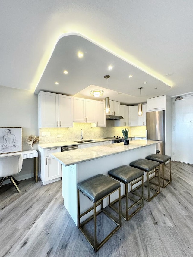 kitchen featuring a kitchen island, white cabinetry, hanging light fixtures, stainless steel fridge, and light wood-type flooring