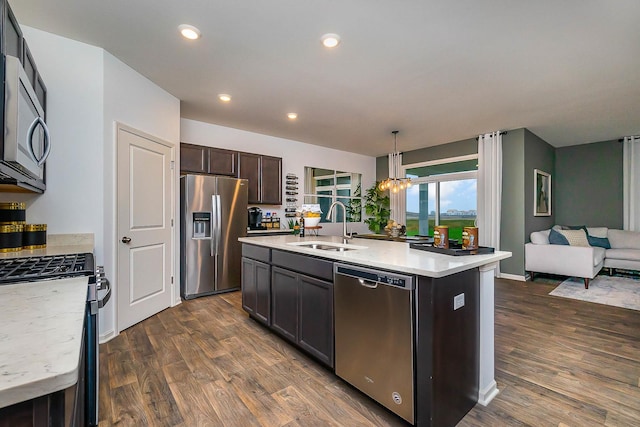 kitchen with pendant lighting, appliances with stainless steel finishes, dark brown cabinetry, an island with sink, and sink