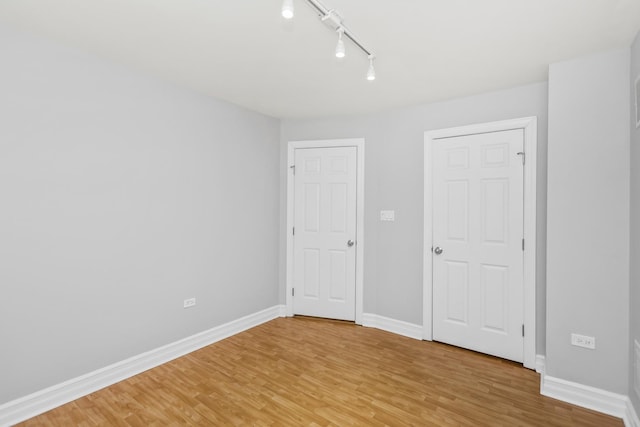 unfurnished bedroom featuring rail lighting and wood-type flooring