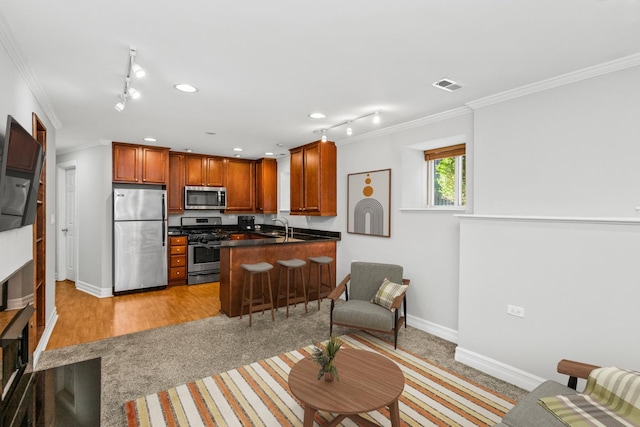 kitchen with appliances with stainless steel finishes, sink, ornamental molding, kitchen peninsula, and a breakfast bar area