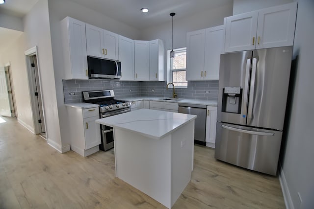 kitchen with a kitchen island, white cabinetry, stainless steel appliances, sink, and hanging light fixtures