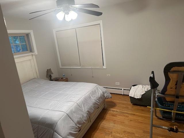 bedroom featuring ceiling fan, a baseboard heating unit, and light hardwood / wood-style flooring