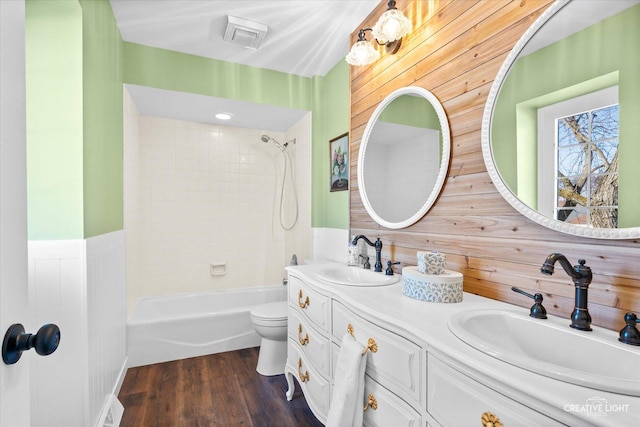 full bathroom with toilet, tiled shower / bath combo, wood walls, wood-type flooring, and vanity