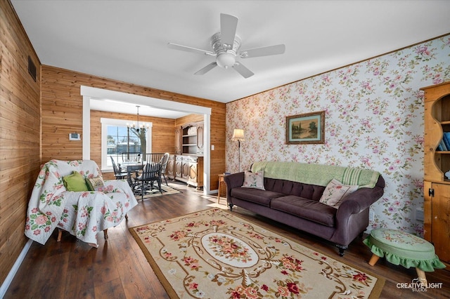 living room featuring ceiling fan with notable chandelier, dark hardwood / wood-style floors, and wooden walls