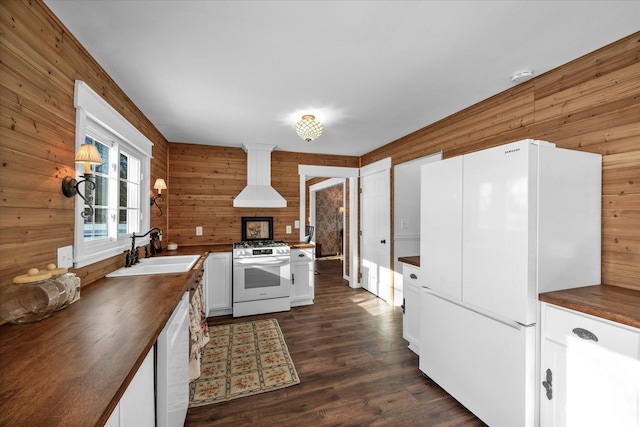 kitchen featuring white appliances, dark hardwood / wood-style flooring, wall chimney range hood, white cabinets, and sink