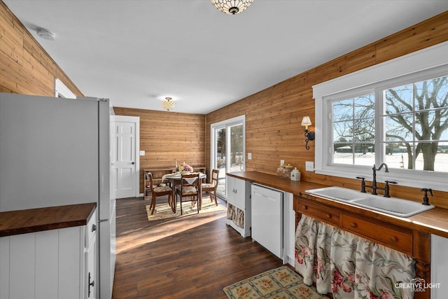 kitchen featuring white dishwasher, dark hardwood / wood-style floors, wooden walls, and sink