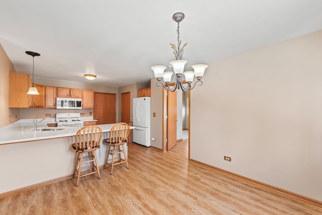 kitchen with sink, hanging light fixtures, light wood-type flooring, kitchen peninsula, and white appliances