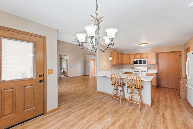 kitchen featuring a kitchen bar, pendant lighting, white appliances, and light wood-type flooring