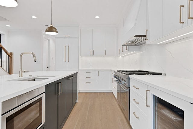 kitchen with pendant lighting, sink, white cabinetry, high end stainless steel range, and beverage cooler