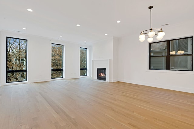 unfurnished living room featuring an inviting chandelier, crown molding, and light hardwood / wood-style flooring