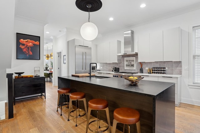 kitchen featuring a center island with sink, ornamental molding, wall chimney exhaust hood, white cabinets, and sink