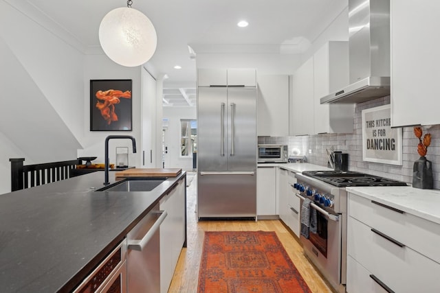 kitchen featuring premium appliances, pendant lighting, wall chimney exhaust hood, white cabinets, and sink