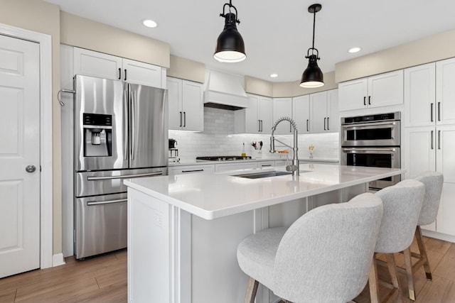 kitchen featuring premium range hood, pendant lighting, sink, white cabinets, and stainless steel appliances