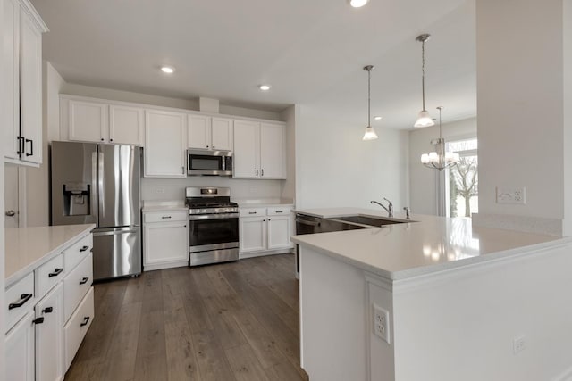 kitchen featuring dark wood-type flooring, sink, white cabinetry, decorative light fixtures, and appliances with stainless steel finishes