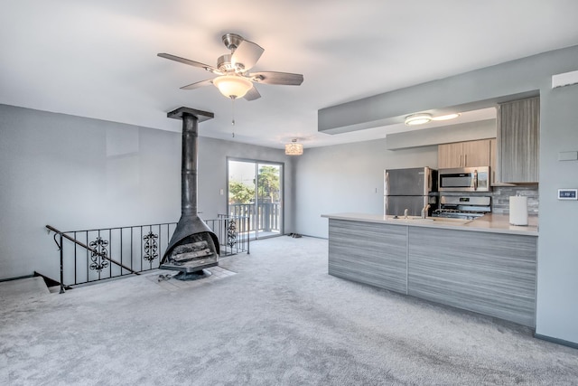 kitchen featuring ceiling fan, backsplash, appliances with stainless steel finishes, a wood stove, and light carpet