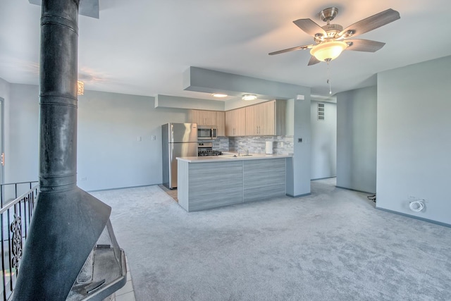 kitchen with ceiling fan, stainless steel appliances, decorative backsplash, a wood stove, and light brown cabinetry