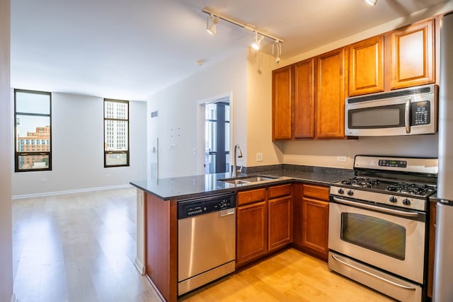 kitchen with kitchen peninsula, sink, light hardwood / wood-style flooring, stainless steel appliances, and rail lighting