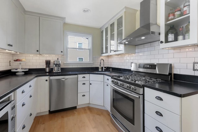 kitchen with appliances with stainless steel finishes, wall chimney exhaust hood, white cabinetry, sink, and light hardwood / wood-style flooring