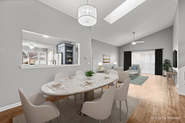 dining area with ceiling fan, wood-type flooring, a skylight, and high vaulted ceiling