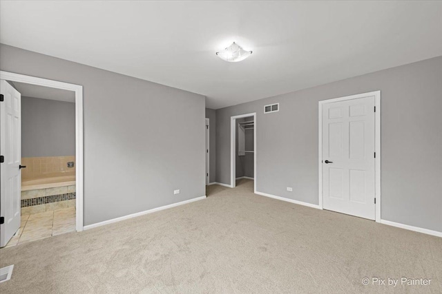 unfurnished bedroom featuring connected bathroom, a spacious closet, light carpet, and a closet