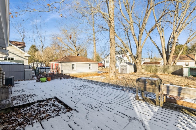 yard layered in snow featuring central AC unit and a storage shed