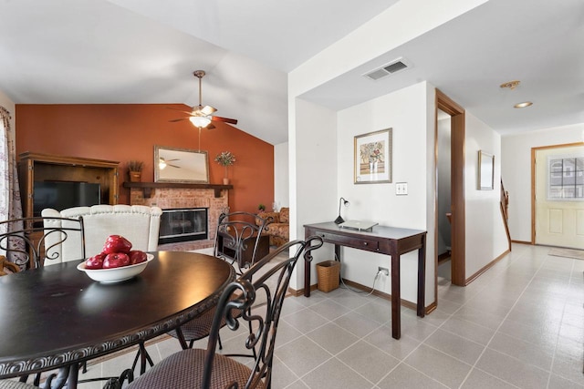 dining space with ceiling fan, a fireplace, visible vents, baseboards, and vaulted ceiling