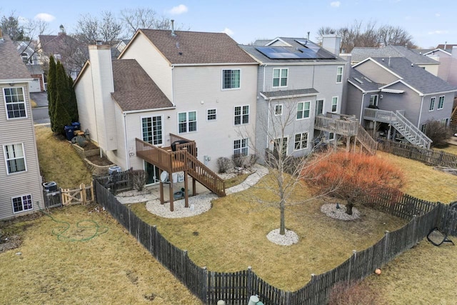 back of house featuring a fenced backyard, a chimney, stairway, roof with shingles, and a yard