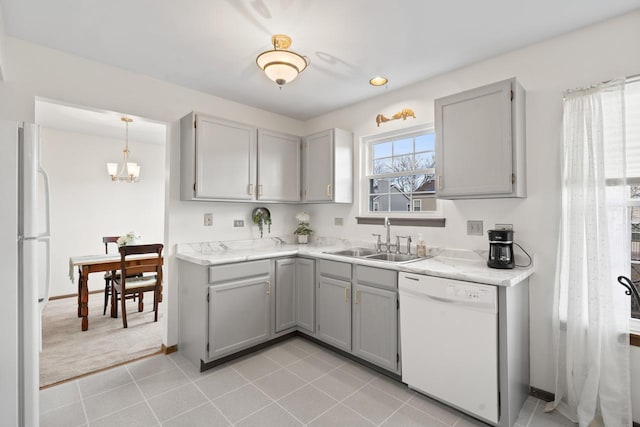 kitchen featuring white appliances, light tile patterned floors, gray cabinetry, a chandelier, and a sink