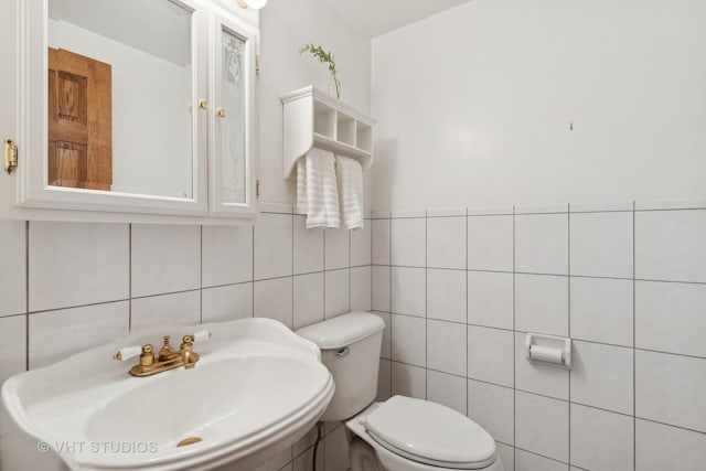 bathroom featuring toilet, sink, and tile walls