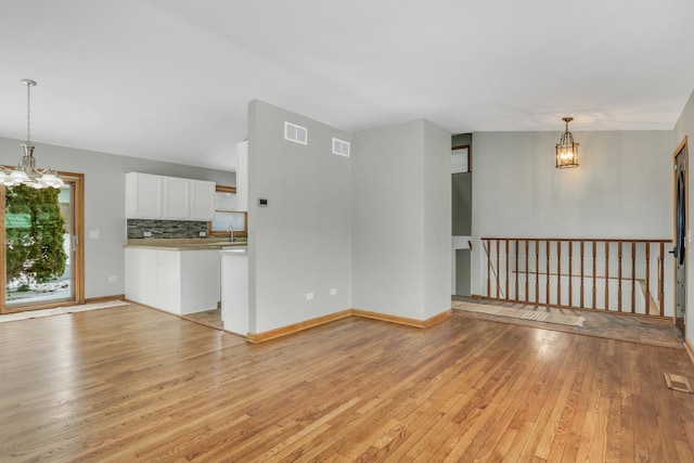 unfurnished living room featuring light hardwood / wood-style floors, sink, and an inviting chandelier