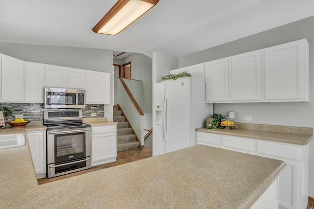 kitchen featuring stainless steel appliances, decorative backsplash, vaulted ceiling, white cabinets, and sink