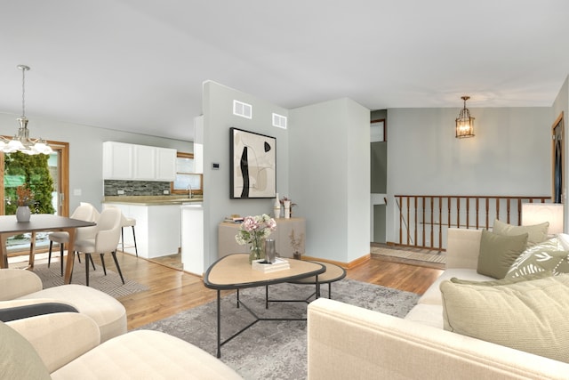 living room with sink, light hardwood / wood-style flooring, and an inviting chandelier