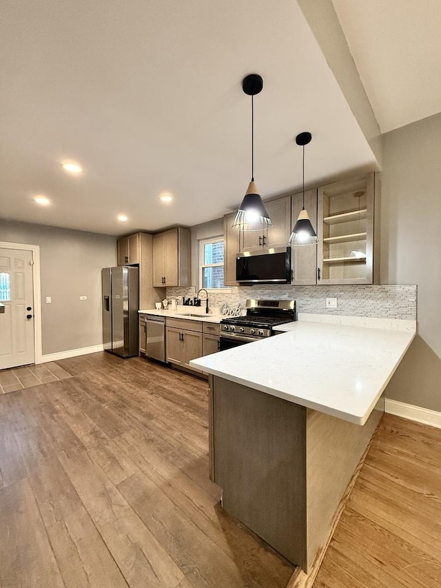 kitchen with appliances with stainless steel finishes, tasteful backsplash, hanging light fixtures, kitchen peninsula, and light wood-type flooring