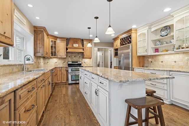 kitchen with premium range hood, sink, appliances with stainless steel finishes, a kitchen island, and white cabinets