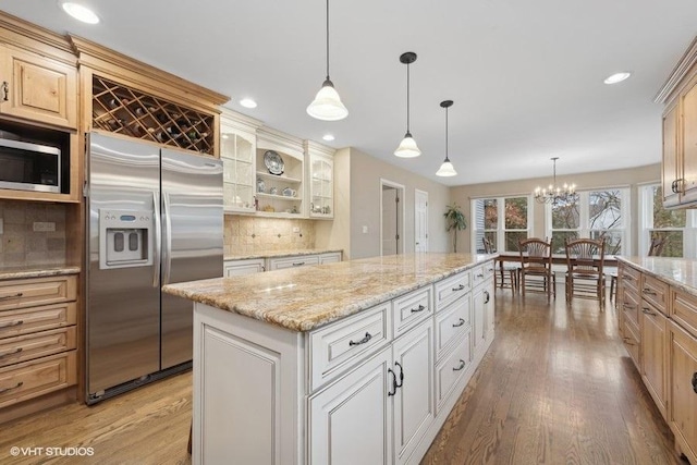 kitchen featuring tasteful backsplash, light wood-type flooring, appliances with stainless steel finishes, a kitchen island, and pendant lighting