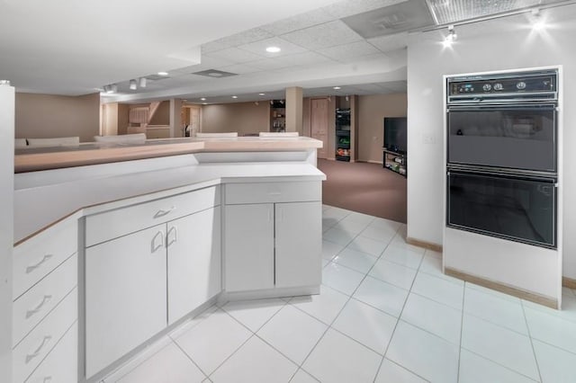 kitchen featuring a paneled ceiling, double oven, white cabinetry, light tile patterned floors, and kitchen peninsula