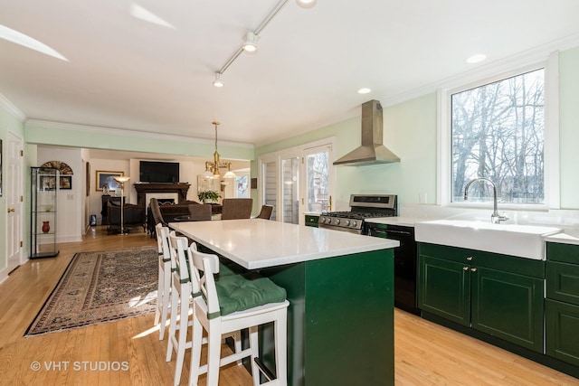 kitchen with stainless steel gas stove, black dishwasher, sink, a breakfast bar area, and wall chimney exhaust hood