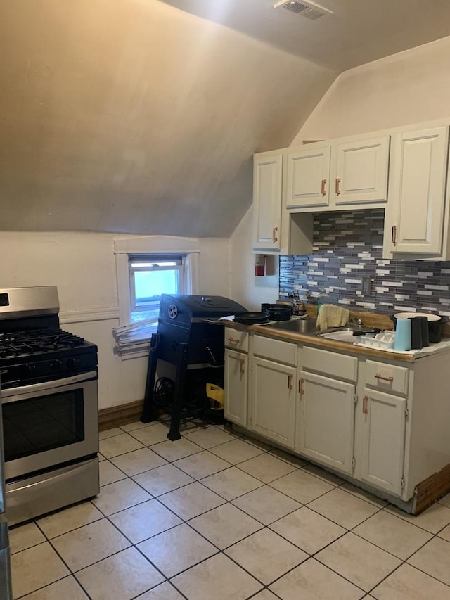 kitchen featuring vaulted ceiling, decorative backsplash, stainless steel gas stove, and white cabinets