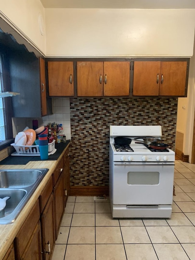 kitchen featuring tasteful backsplash, sink, white gas range oven, and light tile patterned flooring