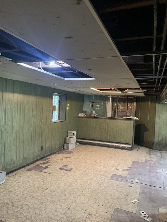 basement featuring a paneled ceiling and wood walls