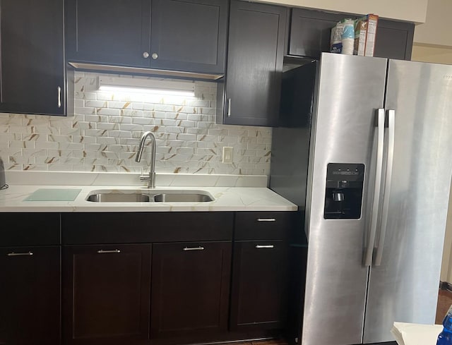 kitchen featuring tasteful backsplash, stainless steel fridge with ice dispenser, light stone counters, and sink